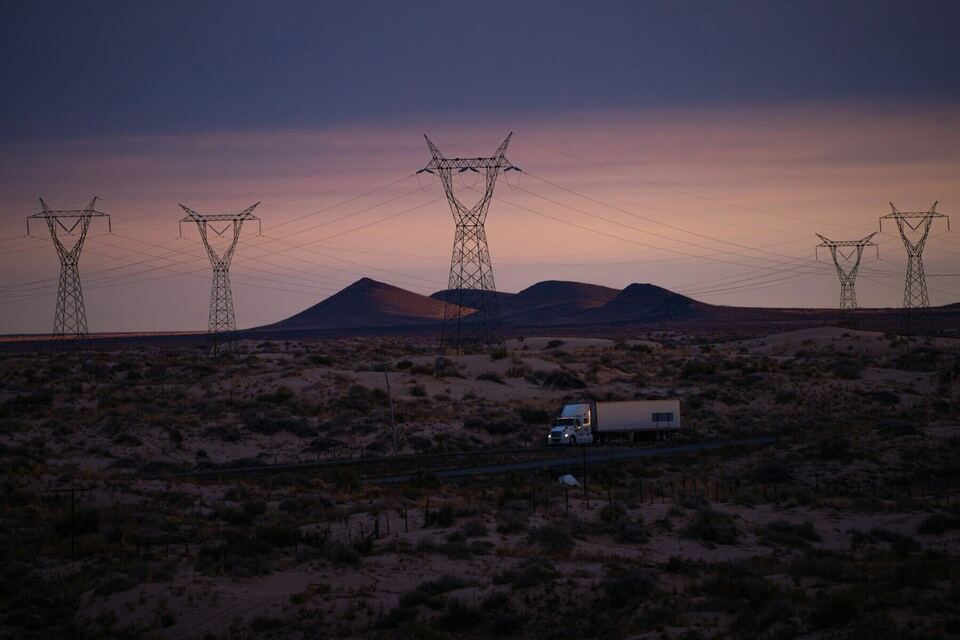 Semi truck crossing desert country beneath power lines at dusk