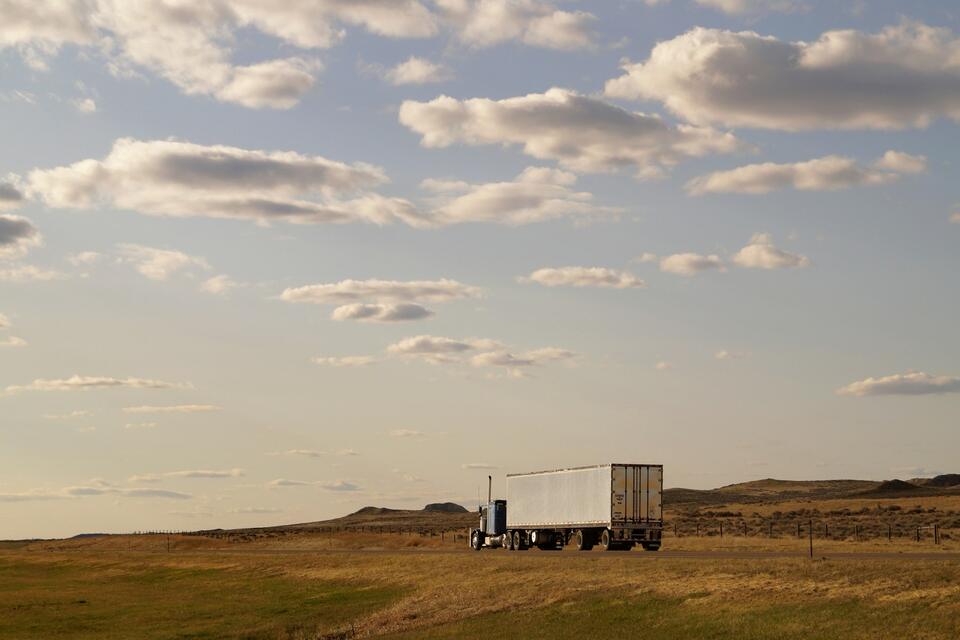 Tractor-trailer with a dry van crossing open prairie under a wide evening sky